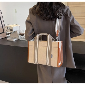 Canvas tote bag with brown leather trim and striped shoulder strap in a cafe setting