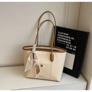 Detail of cream tote bag with brown trim and floral silk scarf on marble surface