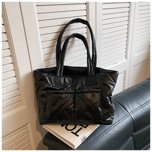 Close-up of a black quilted puffer tote bag with large front pockets on a leather sofa