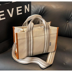 Macro detail of the beige canvas tote bag with brown leather handles on a dark sofa