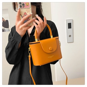 Close-up of yellow leather box bag featuring magnetic closure and fashion text engraving