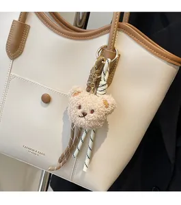 Close-up of cream white tote bag with brown handles and a cute beige plush bear charm