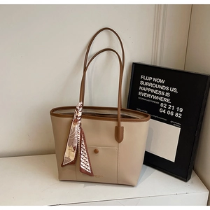 Detailed close-up of the beige tote bag with brown handles and a patterned silk scarf