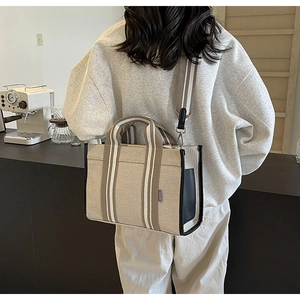Detail of beige canvas tote bag with black trim and striped woven shoulder strap