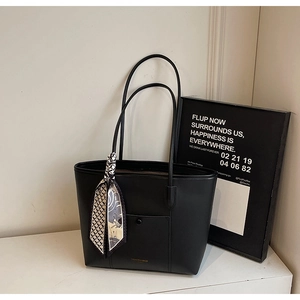 Detail of black leather tote bag featuring a gold fashion logo and decorative silk scarf
