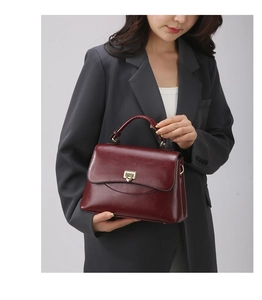Detailansicht der weinroten Lederhandtasche mit glänzendem Finish und goldenem Drehverschluss