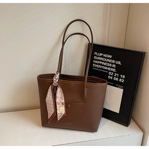 Detail of brown leather tote bag featuring elegant silk scarf and front buckle pocket