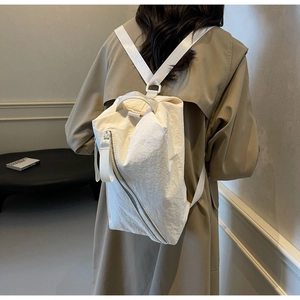 Detail of a white minimalist canvas backpack featuring a unique diagonal zipper design