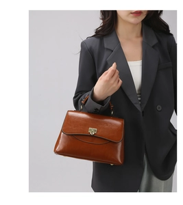 Detail der braunen Lederhandtasche mit goldenem Drehverschluss am grauen Anzug