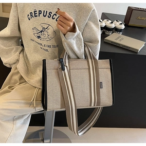 Detail of canvas tote bag with striped straps, side brand tag, and reinforced piping