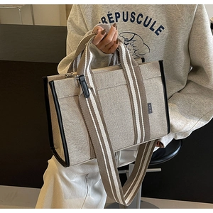 Detail of canvas tote bag featuring premium leather piping and striped shoulder strap