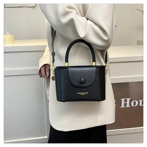 Detail of black leather box bag with round handle and gold hardware on a model
