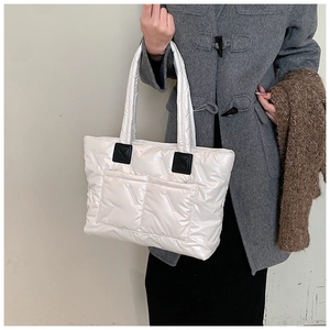 Detailed shot of white quilted puffer tote bag with black patches on gray background