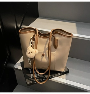 Close-up of color-block tote bag featuring leather front pocket and plush bear charm