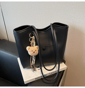 Detail of black tote bag featuring a cute beige plush bear pendant on its handle