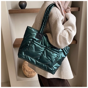 Detailed side view of dark green quilted tote bag with metallic finish on wooden shelf