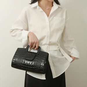 Detail of black crocodile embossed tote bag featuring a round integrated handle