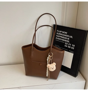 Detail of dark brown leather tote bag with a cute bear charm and woven rope accessory