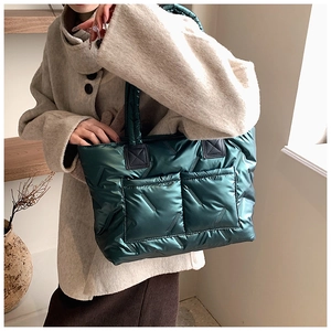 Close-up of a dark green quilted tote bag featuring padded handles and glossy fabric