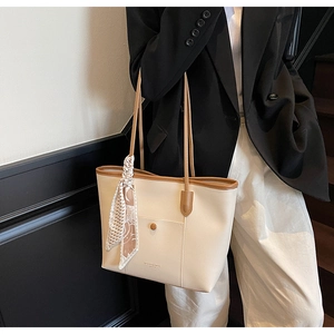 Detail of off-white tote bag featuring brown leather trim and decorative plaid scarf