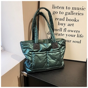 Detail of dark green metallic quilted tote bag with padded texture and side pockets
