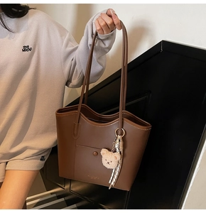 Detail view of large brown tote bag with plush bear charm and silk scarf decoration