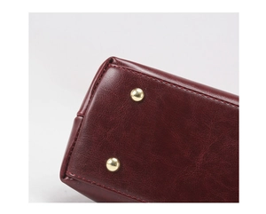 Close-up of wine red leather handbag bottom with gold metal feet and red stitching