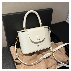 Detail of white structured box bag with hard handle on gift box and knitwear