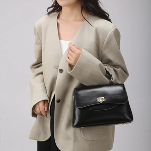 Detail of minimalist black leather tote bag with gold twist lock and elegant crossbody strap