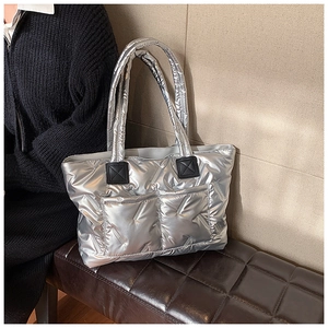Detail of silver quilted tote bag with front pockets and black reinforced handle patches