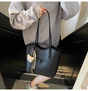 Detail of minimalist black tote bag featuring a front pocket and brown plush bear charm