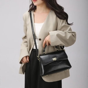 Detail of a black leather handbag with a gold twist lock and woven handle detail on model