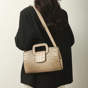 Detail of beige faux crocodile texture and square handle on woman's crossbody tote bag