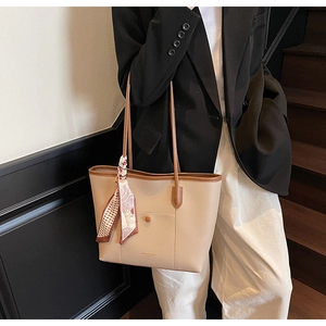Detail of minimalist beige tote bag with brown handles and decorative floral scarf accessory
