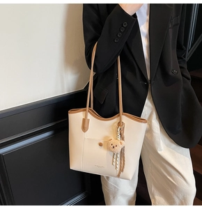 Detail of cream tote bag with brown trim, featuring a cute plush bear charm and metal buckle