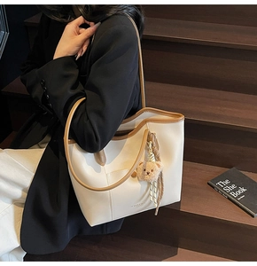 Detail of cream white tote bag featuring brown trim and cute plush bear charm decoration