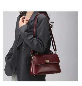 Detail of dark burgundy vintage messenger bag with gold lock on grey blazer outfit