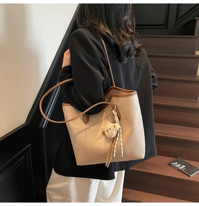 Close-up of beige tote bag with brown trim and cute bear charm in a lifestyle setting