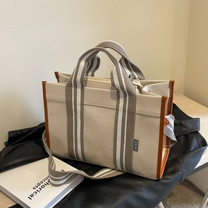 Minimalist canvas tote bag with brown leather trim and striped strap on black jacket