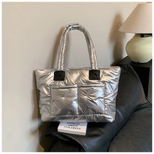 Silver quilted tote bag with front pockets on leather sofa in home setting