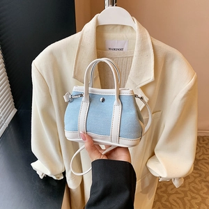 Mini denim crossbody bag with white leather trim and silver metal rivet in hand-held view