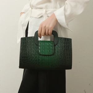 Detail of green crocodile-embossed leather tote bag with U-shaped handle and glossy finish