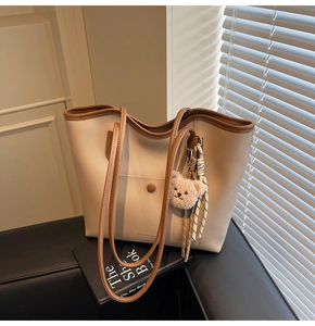 Detail view of large cream tote bag with brown trim and cute plush bear accessory