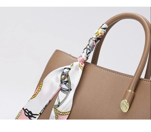 Détail de la poignée en cuir litchi marron avec foulard en soie décoratif et fermoirs dorés