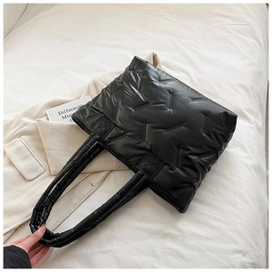 Top view of a black quilted puffer tote bag on a bed with a beige jacket backdrop