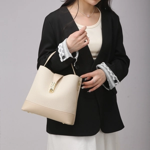 Detail of beige woven fabric bucket bag with smooth leather trim and golden metal buckle