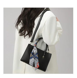 Sac à main noir moderne en cuir avec foulard en soie porté sur un blazer blanc
