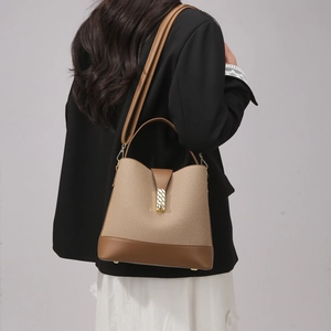 Canvas bucket bag detail with brown leather trim and golden textured lock on black blazer