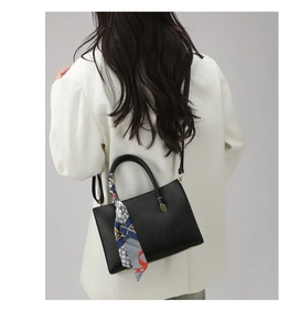 Détail d'un sac à main noir en cuir litchi avec une écharpe décorative en soie imprimée
