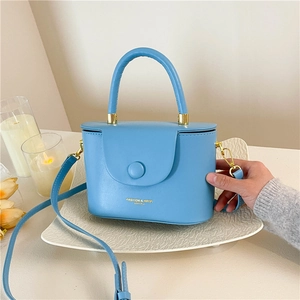 Sky blue minimalist leather box bag with adjustable strap and golden hardware on a tray